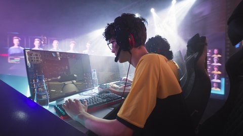 Esportsman gamer in glasses and headphones playing shooter on computer near team while taking park in professional gaming championship battle