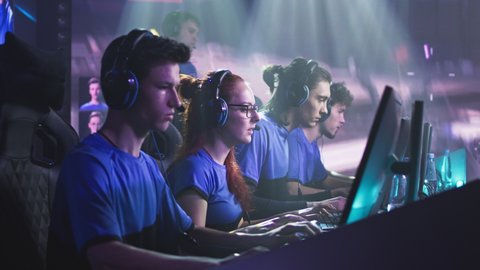 Cheerful young woman gamer esportsman in glasses and headphones smiling and giving high five to male teammates while celebrating victory in video game match during professional tournament