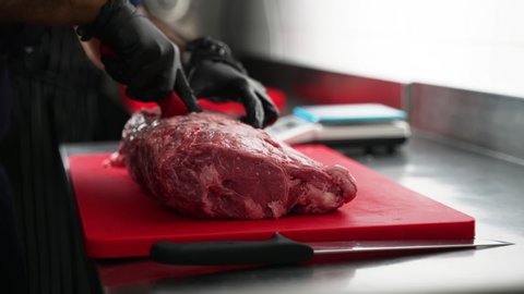 butcher cuts a large piece of selected meat on a steel table