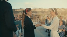 Beautiful Female Queer Couple Exchange Rings and Kiss at Outdoors Wedding Ceremony Near Ocean. Two Lesbian Women in Love Share Their Big Day with Diverse Multiethnic Friends. LGBTQ Relationship Goals. - Powered by Shutterstock - Get 15% off with code: PIKWIZARD15