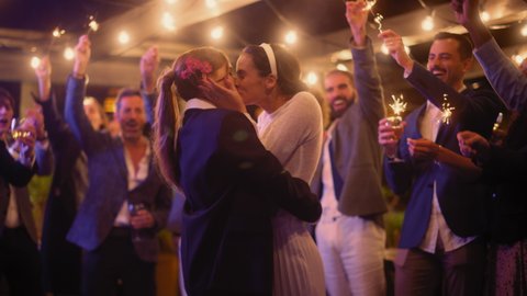 Beautiful Happy Lesbian Couple Celebrate Wedding at an Evening Reception Party with Diverse Multiethnic Friends. Queer Newlyweds Dancing and Kissing at a Restaurant Venue. LGBTQ Relationship Goals.