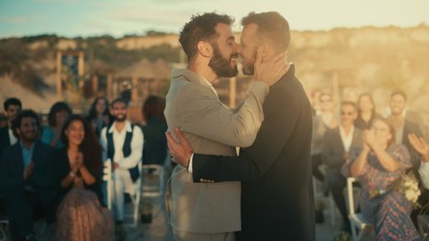 Handsome Gay Couple Exchange Rings and Kiss at Outdoors Wedding Ceremony Venue Near the Sea. Two Happy Men in Love Share Their Big Day with Diverse Multiethnic Friends. LGBTQ Relationship Goals.