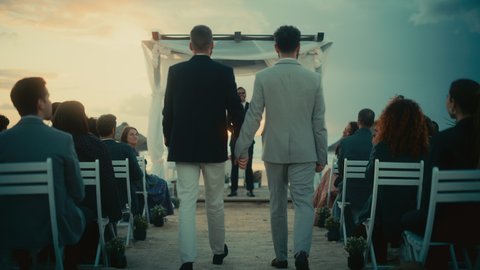 Handsome Gay Couple Walking Down the Aisle at Outdoors Wedding Ceremony Venue Near the Ocean. Two Happy Men in Love Share Their Big Day with Diverse Multiethnic Friends. Cute LGBTQ Relationship Goals.