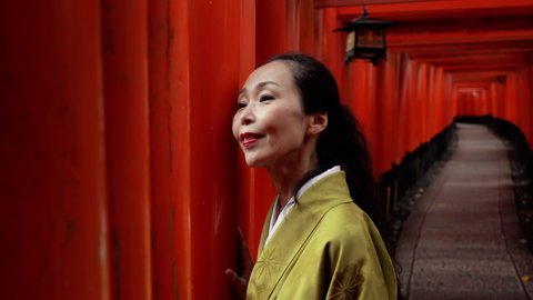Elegant Japanese woman walking along a path lined with Torii Gates.
