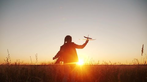 girl kid run in the park across the field play with an toy airplane in his hand a silhouette at sunset wants to astronaut pilot. fun fantasy dream kid fun concept. child run wheat play with toy