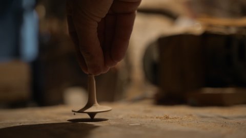 a man's hand unwinds a handcrafted wooden toy whirligig on a wooden table against the background of a workshop, yula spins and stops