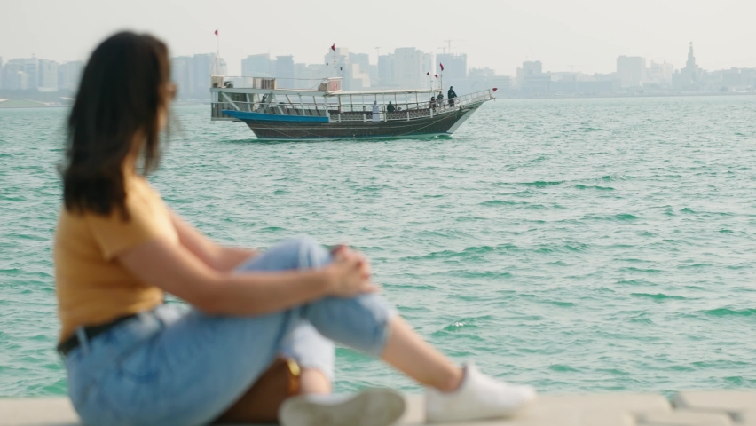 Tourist woman at corniche watching dhow boat passing on west bay at Doha Qatar
