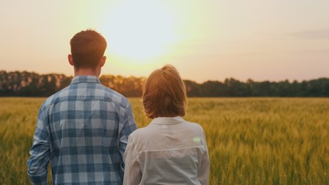 Two farmers - a man and a woman look at a wheat field, view from behind