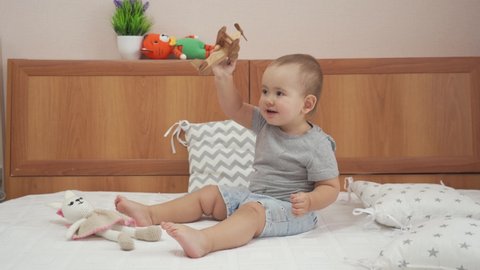 A newborn girl 15-20 months old is playing with a wooden toy airplane while sitting on her parents' bed in the bedroom