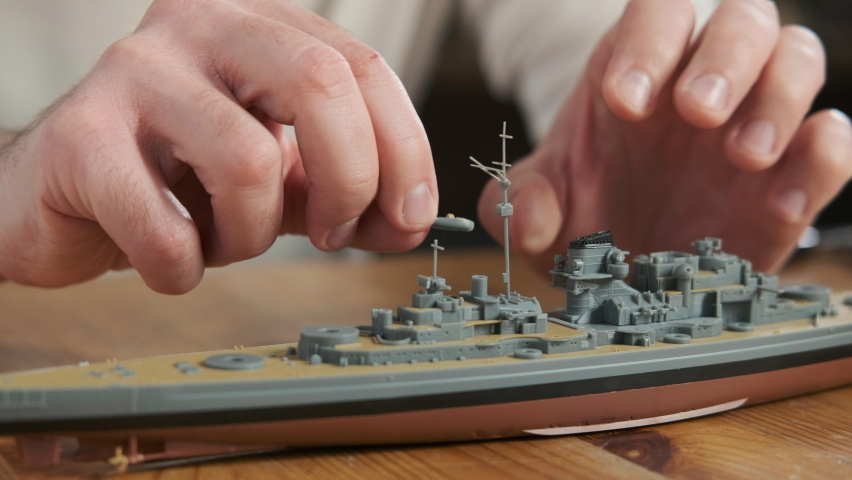 Happy adult male assembler plastic model of warship according to drawings and instructions. Closeup of man gluing elements to layout with hands. Passion for modeling and building toys.  Scale Modeling Royalty-Free Stock Footage #1086008573