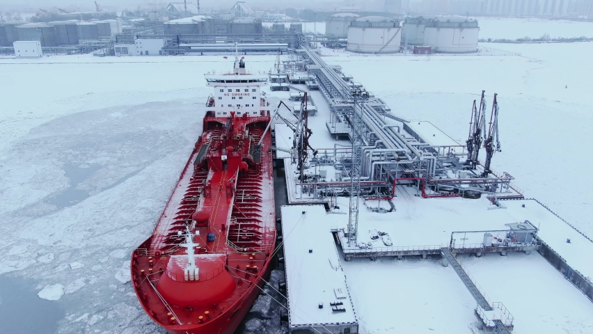 A large red ship tanker stands at the pier in the port and refuels in winter in the midst of snow and ice, aerial view Royalty-Free Stock Footage #1086008747