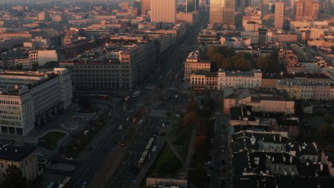 Slide and pan aerial footage of roundabout. High rise office tower illuminated by bright rising sun in background. Warsaw, Poland