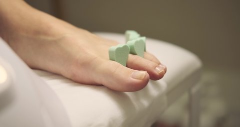Pedicurist applying nail polish to foot finger nails of woman