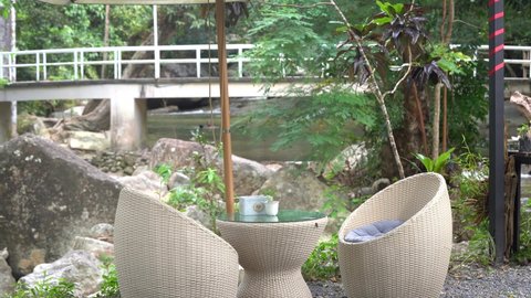 A Tropical Café By The River With Rattan Garden Conversation Rounded Table And Chairs With Bridge In The Background, Koh Samui, Thailand. - Medium Shot