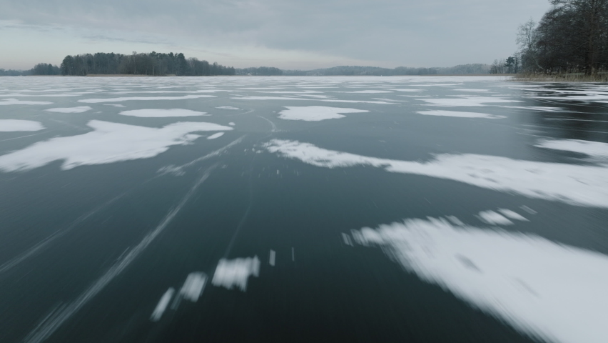 Frozen Lake with snow patterns from low wide angle fast flying Mavic 3 Cine drone. Filmed in prores at 50fps. Winter daytime. Ice clouds ant trees in horison visible.