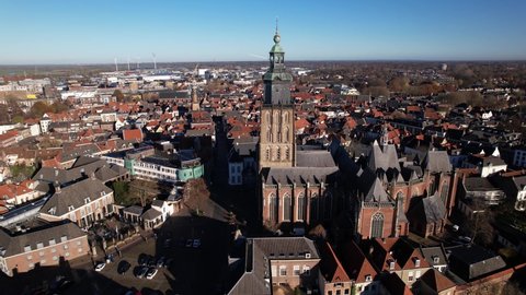 Aerial pan around Walburgiskerk church in picturesque Hanseatic tower town of Zutphen in The Netherlands showing its rooftops and position in the historic city center with river IJssel passing by