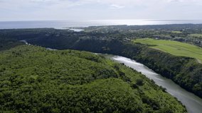 Aerial backward over forest along Chavon river with village and sea in background, La Romana in Dominican Republic
