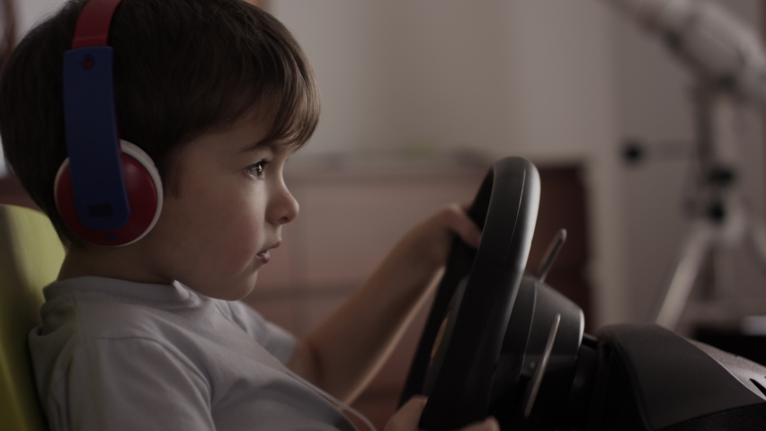 Boy Playing Racing Video Game in Game Console. Child Playing Computer Game in Headphones With Steering Wheel. Gamer With Headset Holding Steering Wheel Playing Video Game. Kid Gambling Addiction. Royalty-Free Stock Footage #1086039941