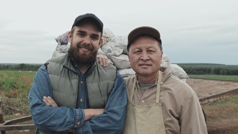 Horizontal medium portrait of modern farm workers standing against sacks of potatoes smiling at camera