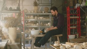 Couple of potters, happy woman and man, are working together in large pottery studio, man is making new clay item, woman has video call, pleasant working day, Slow motion.