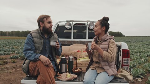 Zoom in shot footage of young adult man and woman sitting relaxed on pickup truck cargo having lunch break