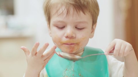 Boy eating borscht spoon in baby chair in kitchen