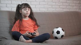 Football on play station. A little fan has a leisure with a console in the room. A cute little girl is playing with a prefix.