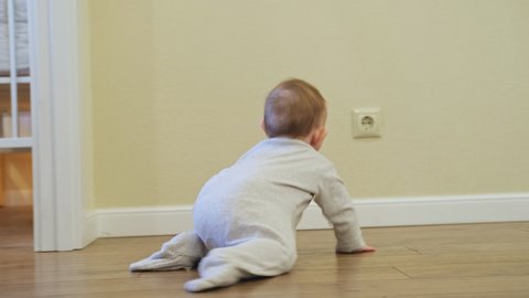 Baby toddler reaches into the electrical outlet on the home wall with his hand. Danger and protection of child fingers from electric shock