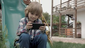 Child using smart phone online on the playground. Boy playing video game on portable device outdoors. Social media, app on mobile phone. Childhood concept.