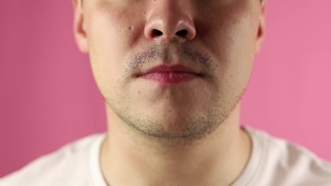 A young man on a pink background paints his lips with red lipstick, close-up. The man paints his lips, smacks his lips and sends a kiss at the end.
