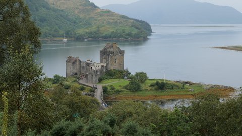 Very old Eilean Donan Castle, Scotland, UK at Loch Duich shore from the top of the hill above Dornie village with unrecognizable tourists