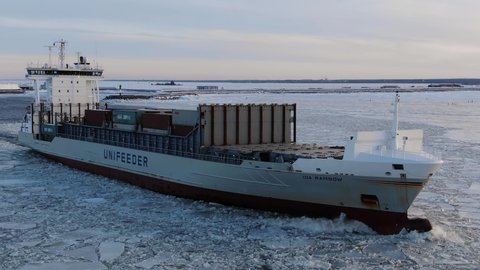 A large cargo ship with containers floats on the sea in the middle of the ice in winter, aerial view. Russia, St. Petersburg, January 2022