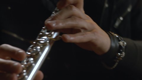 Male hands hold a flute. The musician plays in the orchestra. Classical music in live performance