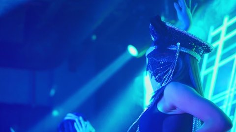 Close-up from the back of a dancing girl in a nightclub with a mask on her face.