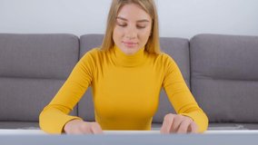 Beautiful freelancer woman typing on laptop computer at home during lockdown. Attractive young adult female working online with cheerful smile. White person doing distant work with internet connection