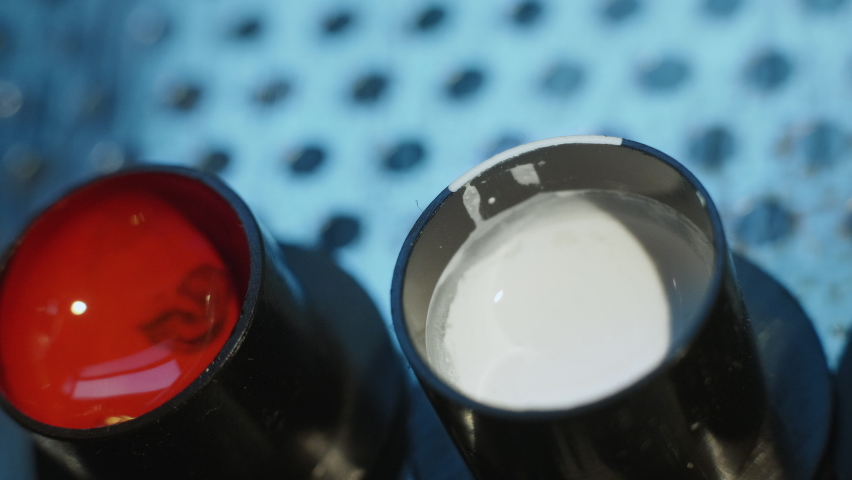 Close-up view of tattoo studio, artist loads magnum needles bar with liquid white color ink from fixed with vaseline cap. Tattooing machine preparation. Ivory dye paint fluid filling in tattooist gun.