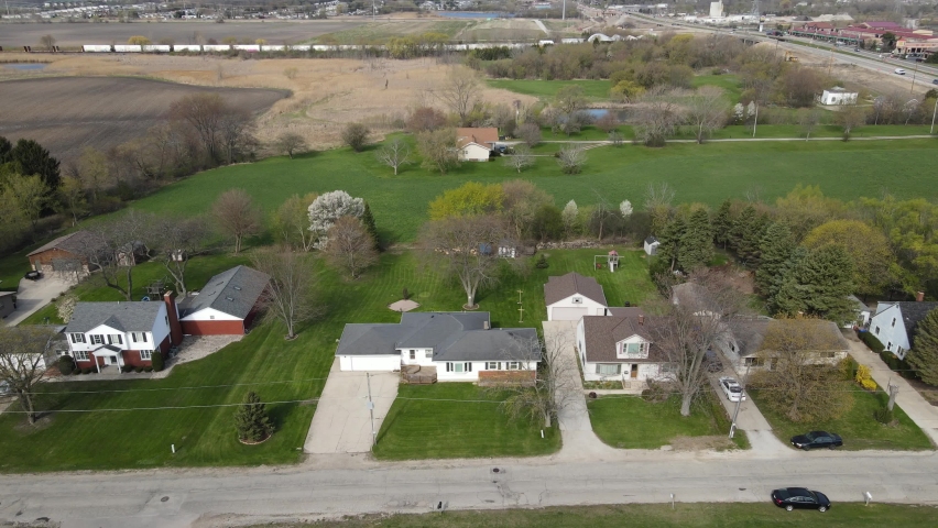 Aerial view of rural farm land and homes with water and train tracks in the distance. Highway and business section in the background. 