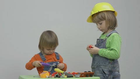 Two children equipped with protection helmet and overall play at tools table, construction team, conceptual