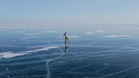 Aerial view of man skating on lake Baikal covered by ice. Male sportsman ejoying sport in cold weather with sky and clouds reflected in beautiful icy surface of lake.