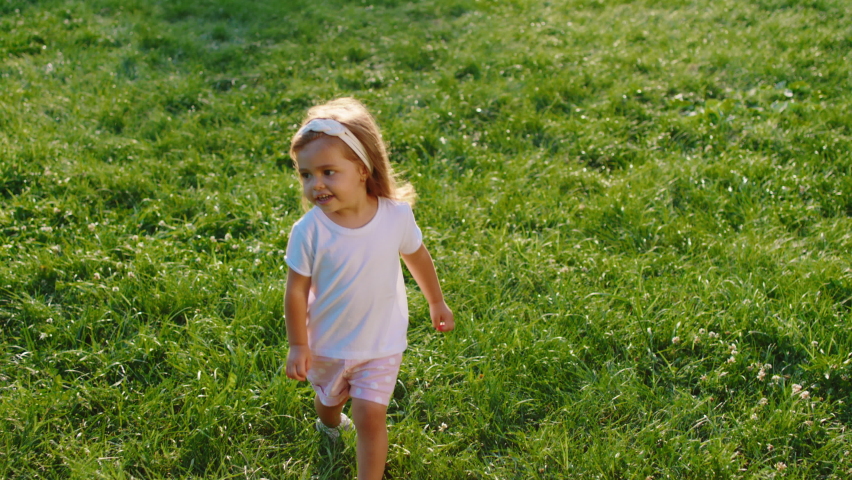 Very charismatic little girl in front of the camera with a happy face playing on the grass in the middle of the park