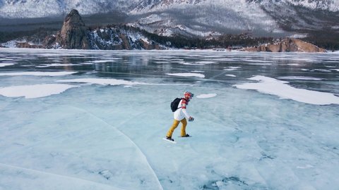 Aerial view of man skating on lake Baikal covered by ice. Male sportsman ejoying sport in cold weather with sky and clouds reflected in beautiful icy surface of lake.