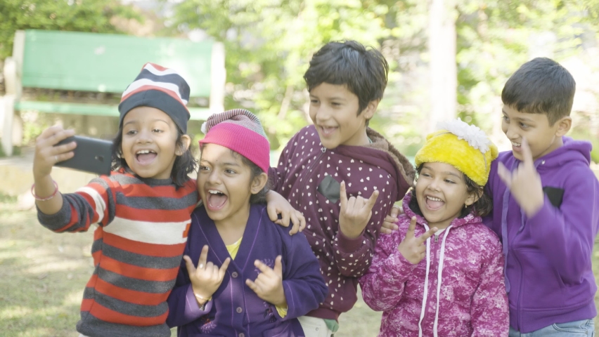 Excited teenager indian kids posing or taking selfie on mobile phone at park - concept of togetherness,holidays entertainment and hapiness.