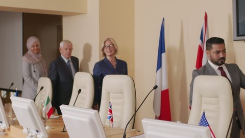 Medium shot of diverse male and female political leaders of different countries arriving at press conference, greeting audience in tabletop microphones
