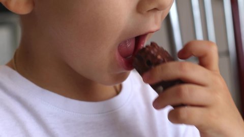 The boy eats chocolates at home in the kitchen. Junk food, childhood concept. In room.