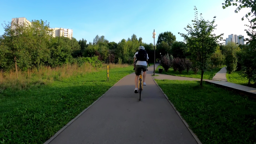 Cyclist rides on a path in a park in the summer among the trees. Back view