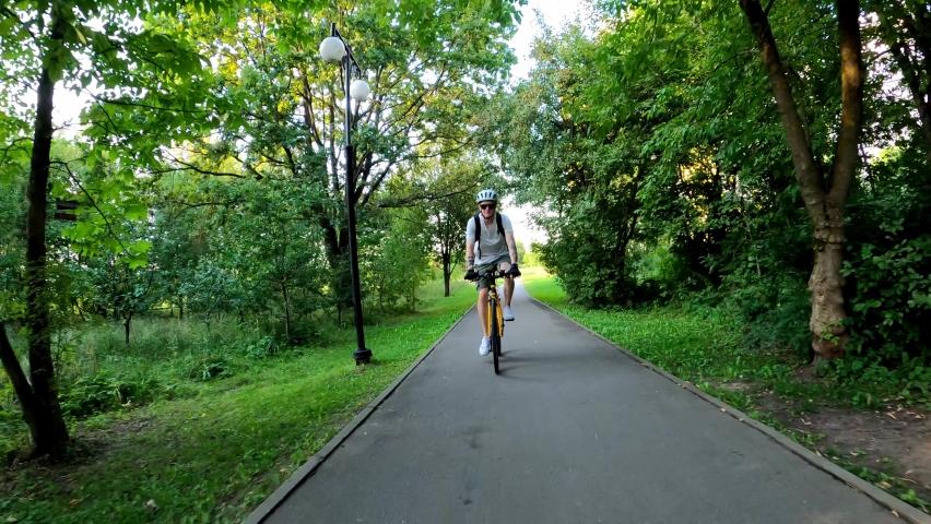 Cyclist rides on a path in a park in the summer among the trees. Front view