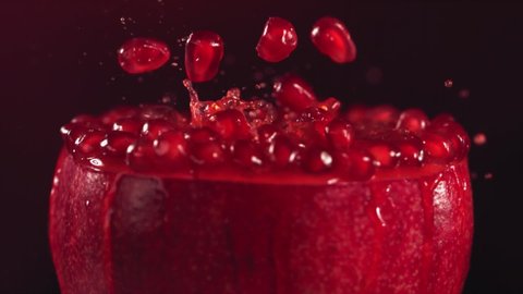 Pomegranate Grains falling on surface of half pomegranate in slow motion