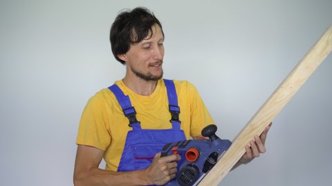 A man professional tile installer a wooden plank and an electric planer in his hands. He looks at the camera smiling
