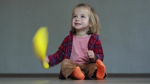 Toddler in a red checkered shirt playing with skittle and laughing. Kid fooling around with toys. Little boy taps toy on the floor and smiles. Kid with beautiful smile in living room.

