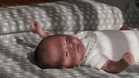 Newborn baby moving while lying on his back on a bed.